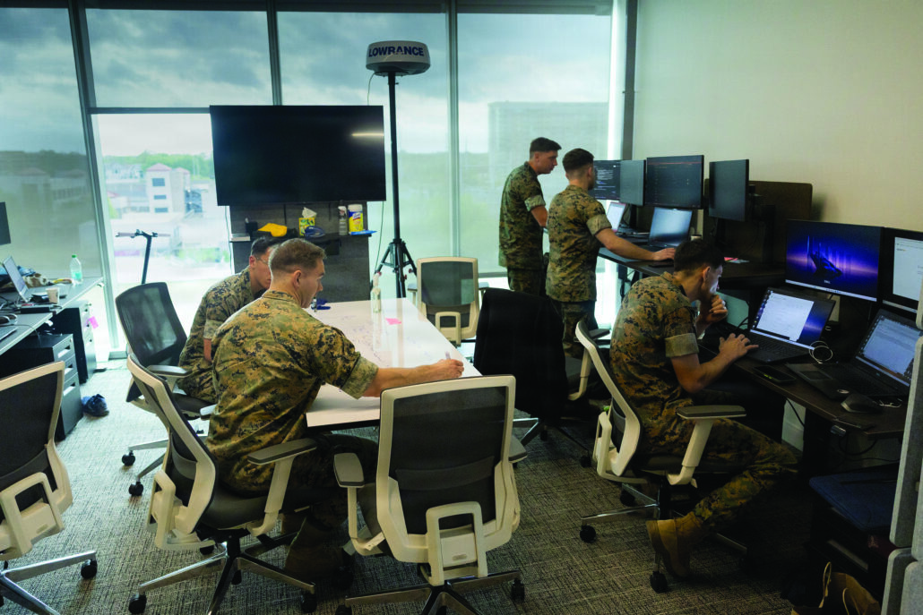 Marines with the Marine Innovation Unit gather in a building with computers and white board tables to work on coding.